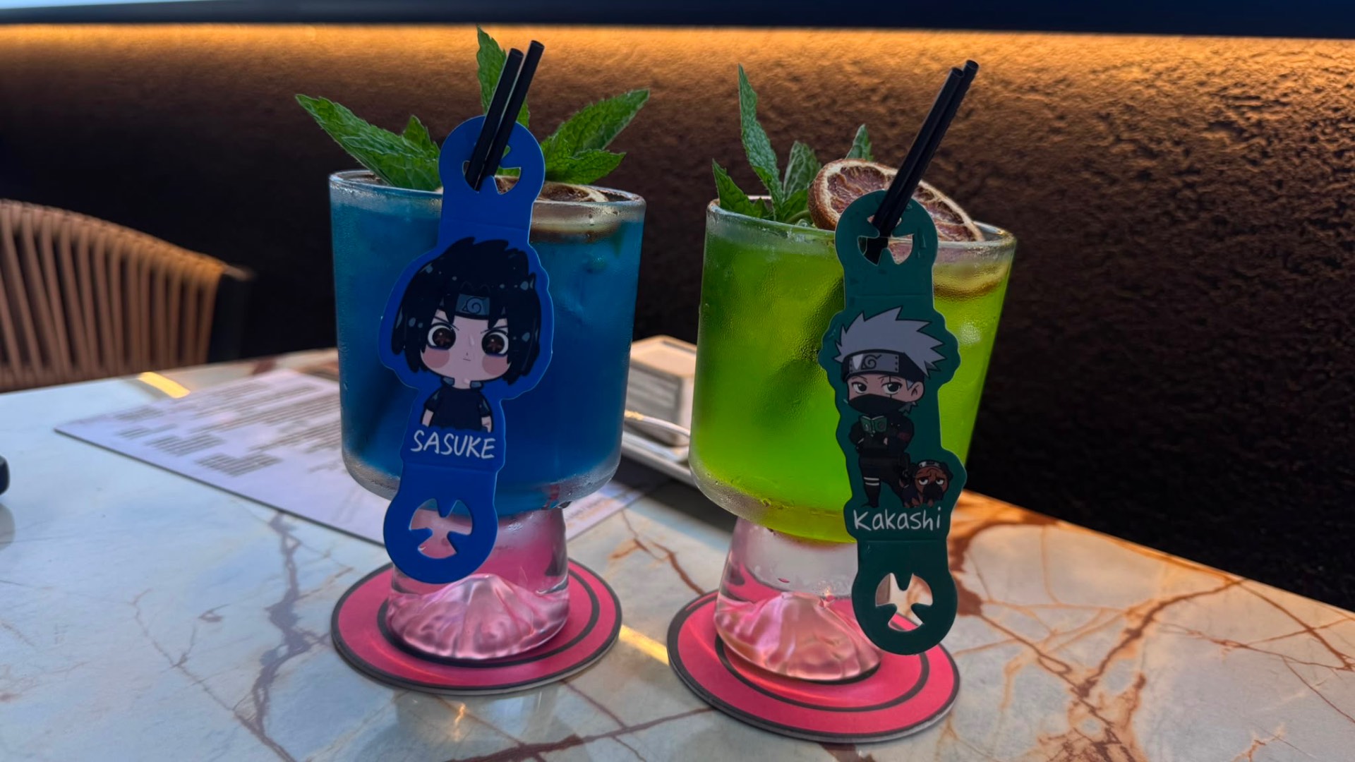Sasuke blue and Kakashi green cocktails with anime charms on a marble table